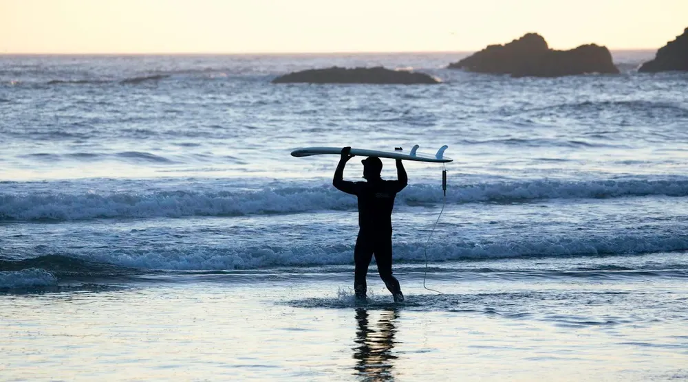 Silhouette d’un surfeur portant sa planche face aux vagues